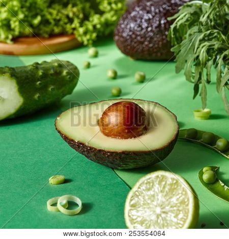 The half of avocado with bone in the focus and other green vegetables for cooking fresh natural vegetarian salad. Detox diet food.