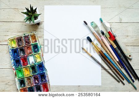 Artist Paint Brushes And Watercolor Paintbox On Wooden Background With Empty Sheet Of Paper. Instrum