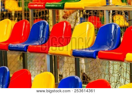 Multicolored Empty Plastic Chairs In The Stands Of The Stadium. Many Empty Seats For Spectators In T