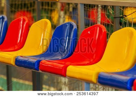Multicolored Empty Plastic Chairs In The Stands Of The Stadium. Many Empty Seats For Spectators In T