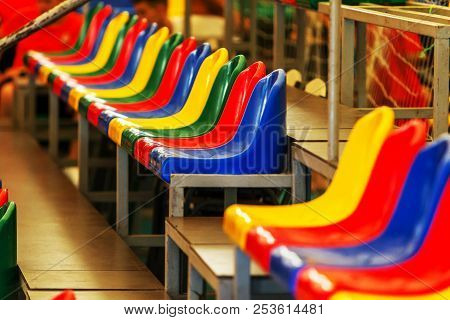 Multicolored Empty Plastic Chairs In The Stands Of The Stadium. Many Empty Seats For Spectators In T