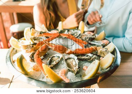 Close-up of fresh oysters and crabs served on ice with slices of lemon at the table of a romantic young couple eating at restaurant
