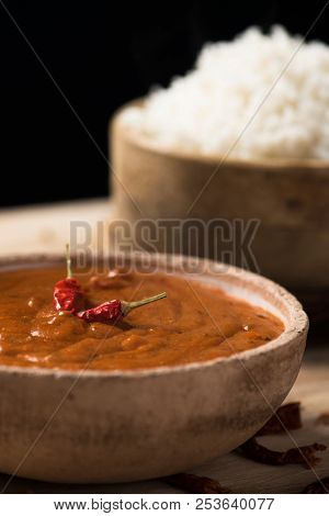 closeup of a bowl with a chicken korma curry and a bowl with cooked rice on a rustic wooden table