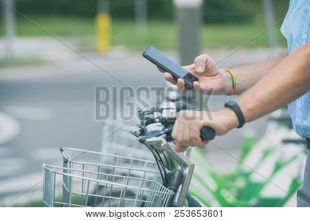 Man is using smart phone to rent bicycle from urban bicycle sharing station