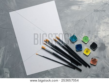 Painting Brusches, White Paper And Watercolors On Gray Concrete Background. Flat Lay, Top View