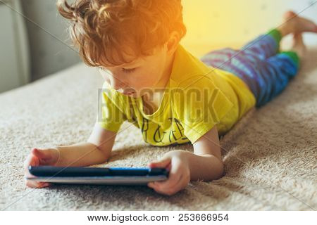 Little Cute Boy In A Green T-shirt Playing Games On A Tablet And Watching Cartoons. Addiction Concep