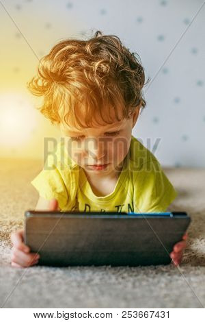 Little Cute Boy In A Green T-shirt Playing Games On A Tablet And Watching Cartoons. Addiction Concep