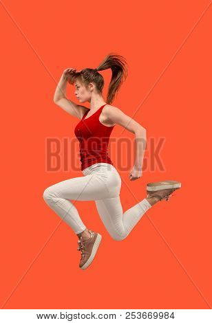 Freedom In Moving. Mid-air Shot Of Pretty Happy Young Woman Jumping And Gesturing Against Orange Stu