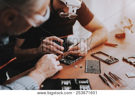 Two Men Repairing Hardware Equipment In Workshop. Repair Shop. Young And Old Workers. Digital Device