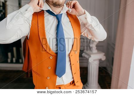 Cropped Shot Of Unrecognizable Male Groom Ties Tie, Dressed In Elegant White Shirt And Orange Jacket