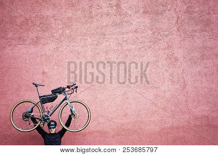 Young Man Handing Gravel Bicycle Over Head Near The Pink Wall