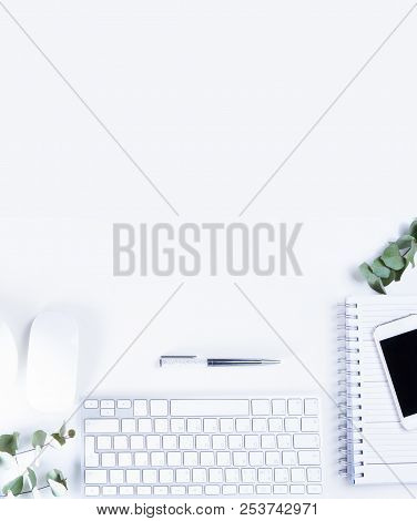 Flat Lay Home Office Workspace With White Modern Keyboard, Notebook And Silver Green Eucaliptus Twig