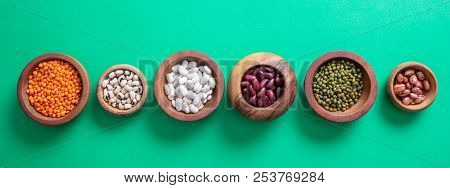 Assortment Of Legumes In Wooden Bowls On Green Background, Isolated, Top View, Banner.