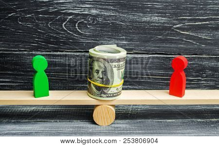 Wooden Figures Of People On Scales And Dollars Between Them. A Dispute Between Two Businessmen. Tria