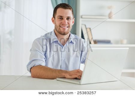 Smiling businessman with rolled up sleeves on his laptop in his home office