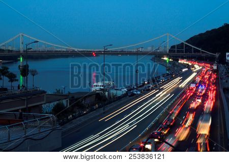 Parkovyi Bridge, which is illuminated with lights in the evening in Kiev with a road and cars near i