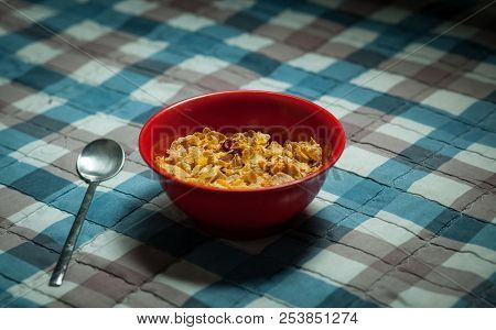 Still Life Of A Metal Spoon And A Red Deep Dish In The Center Of The Frame On A Background Of Violet