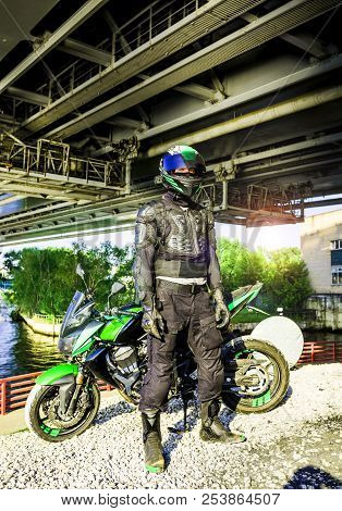 Motorcyclist In A Helmet And In A Protective Suit Stands Under T