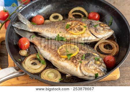 Dorada Fried In A Pan With Onions, Lemon And Cherry Tomatoes