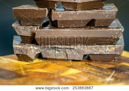 Dark Chocolate Bars Stacked Up With Dark Background In The Ktichen Sitting On Wooden Cutting Board