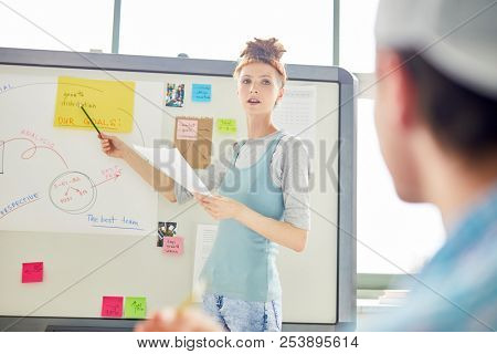 Confident student pointing at yellow paper on whiteboard while looking at groupmate and voicing her ideas