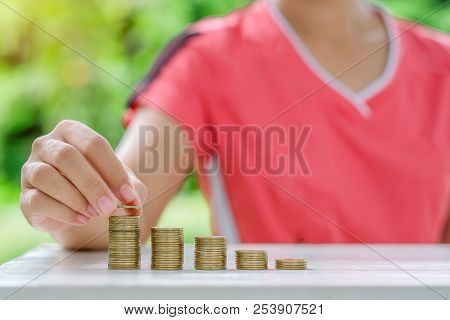 Woman Hand Putting Coin, Gold Coins Stack On Wooden Table In The Morning Sunlight. Business, Investm