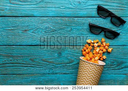Paper cup with popcorn and 3D glasses on blue background. Top view.