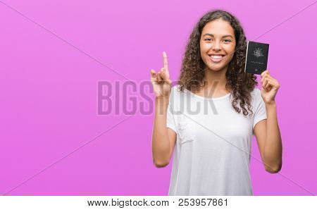 Young hispanic woman holding passport of Australia surprised with an idea or question pointing finger with happy face, number one