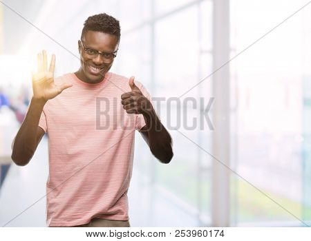 Young african american man wearing pink t-shirt showing and pointing up with fingers number six while smiling confident and happy.