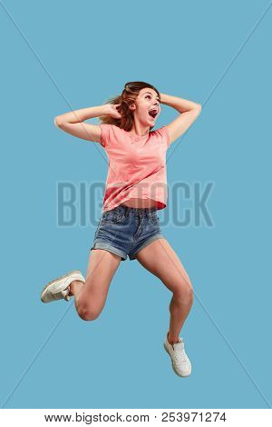 Freedom In Moving. Mid-air Shot Of Pretty Happy Young Woman Jumping And Gesturing Against Blue Studi