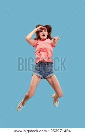 Freedom In Moving. Mid-air Shot Of Pretty Happy Young Woman Jumping And Pointing By Finger Against B