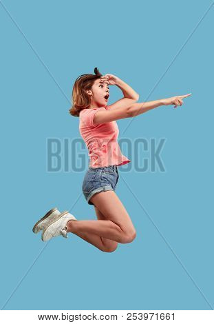 Freedom In Moving. Mid-air Shot Of Pretty Happy Young Woman Jumping And Pointing By Finger Against B