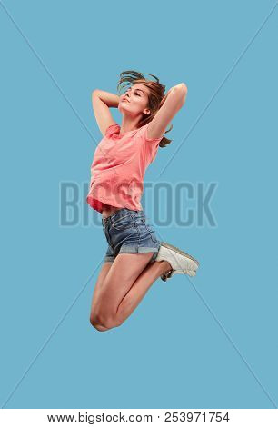 Freedom In Moving. Mid-air Shot Of Pretty Happy Young Woman Jumping And Gesturing Against Blue Studi
