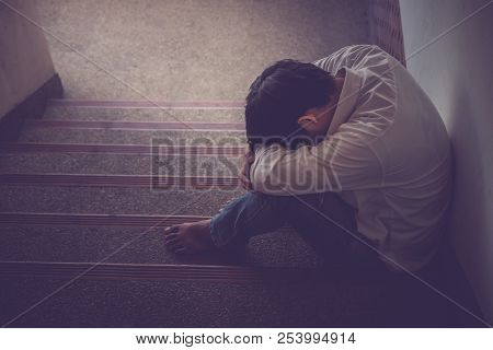 Depressed Man Sitting Head In Hands On The Stairs In Building. With Low Light Environment, Dramatic 