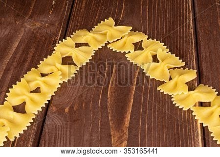 Lot Of Whole Yellow Pasta Farfalle Pieces On Brown Wood