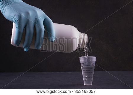 A Gloved Hand Pours Liquid Into A Measuring Cup.