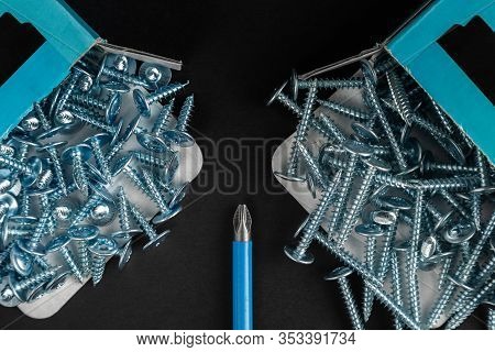 Assortiment Of Bunch Of Sillver Screws From Box With Screwdriver On Black Background. Top View