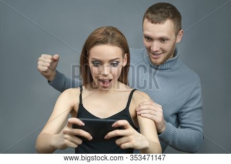 Man With The Girl Excitedly Looking At The Smartphone In An Agitated State. Emotions Of Experiencing