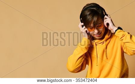 Young Positive Teen Boy In Yellow Hoodie, Sunglasses And Headphones Standing And Smiling Over Yellow