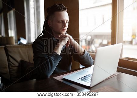 Young Businessman With Dreadlock Having Doing His Work In Cafe Near The Big Window With Laptop. Yout