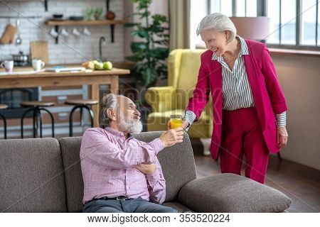 Lady In Bordeaux Siut Giving A Glass Of Juice To His Husband