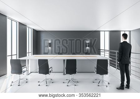 Businessman Standing In Contemporary Conference Room Interior With Copy Space On Gray Wall. Workplac