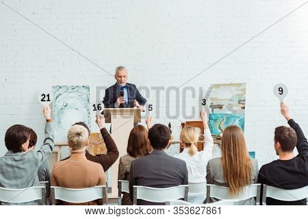 Auctioneer Talking With Microphone And Looking At Buyers With Auction Paddles During Auction