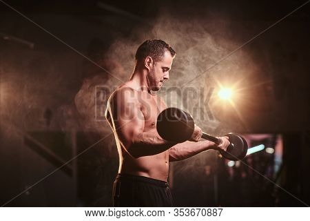 Powerful Mucular Sportsman Doing Weightlifts With Barbell And Looking Concentrated In A Dark Gym Sur