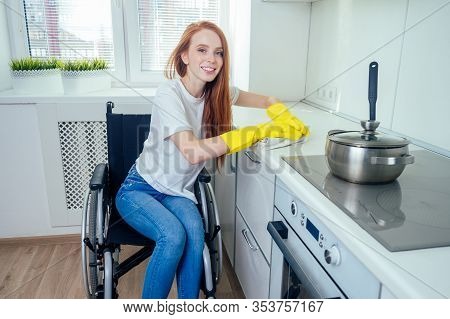 Young Redhaired Ginger Disabled Woman In Wheelchair Wearing Yellow Ribon Gloves And Cleaning Apartme