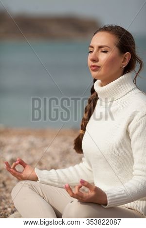 Cute Girl Sitting In The Lotus Position, Meditating, On The Beach. Copy Space. Concept: Yoga, Health