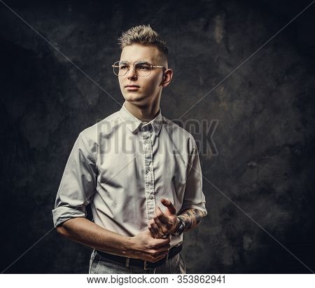 Young Serious Looking Adult Student Guy In A White Shirt With Tattoos On His Hand Posing In A Dark S