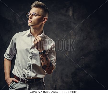 Handsome Guy In A White Shirt With Tattoos On His Hand Posing In A Dark Studio, Looking Decisive And