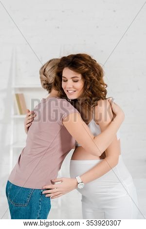 Smiling Pregnant Woman Hugging Doula In Living Room