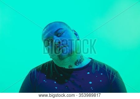 Threat. Portrait Of A Guy With Colorful Neon Light On Green Studio Background. Male Model With Calm,